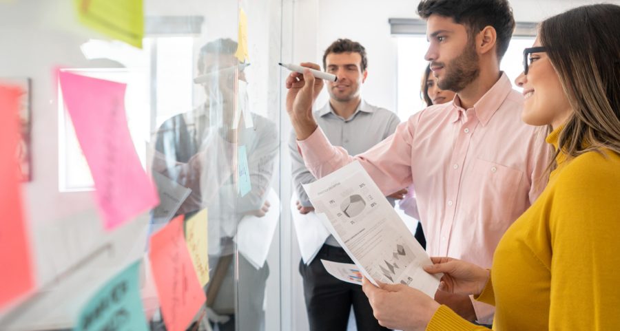 Business team creating a marketing strategy at the office and writing ideas on a glass board - teamwork concepts