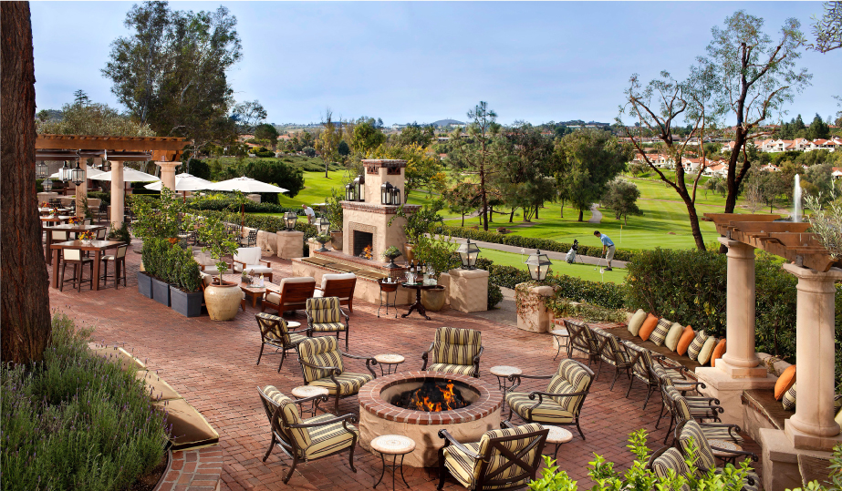 A large patio with chairs around a fire pit with a golf course in the background.