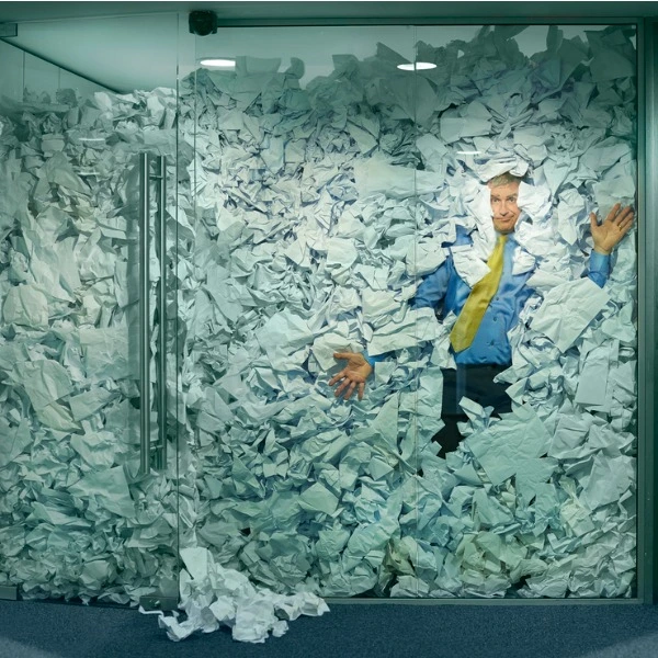 man in glass office filled with papers