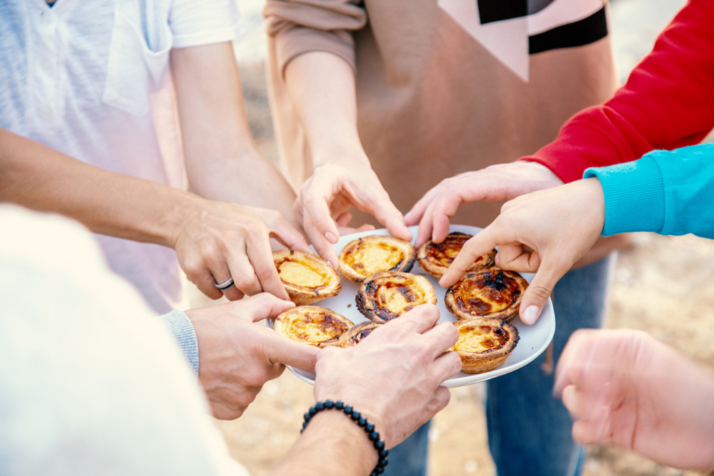 Group of people take pashtel de nata traditional Portuguese dessert with plate